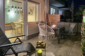 Ein Außenbereich mit Terrasse, Sitzgelegenheiten, einem Hängesessel und einem Tisch mit Kerze.