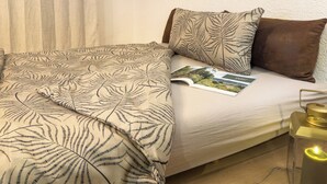Ein Bett mit einem gemusterten Bettüberwurf, einer Zeitschrift und einer Kerze in einem Glasgefäß.