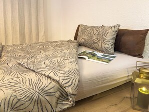 Ein Bett mit einem gemusterten Bettüberwurf, einer Zeitschrift und einer Kerze in einem Glasgefäß.