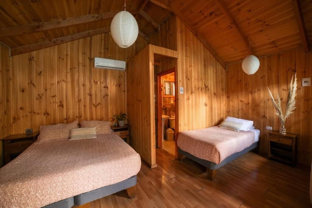 Un dormitorio de cabaña de madera con dos camas, techo de madera y una ventana pequeña.