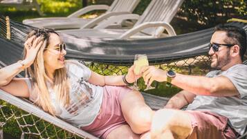 Un hamac où sont allongées deux personnes, une zone herbeuse et, au fond, une rangée de chaises longues vides.