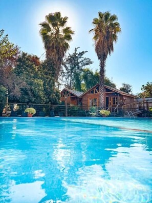 Une piscine dotée d’une terrasse en bois, entourée de palmiers et bordée d’un bâtiment au toit en pente.