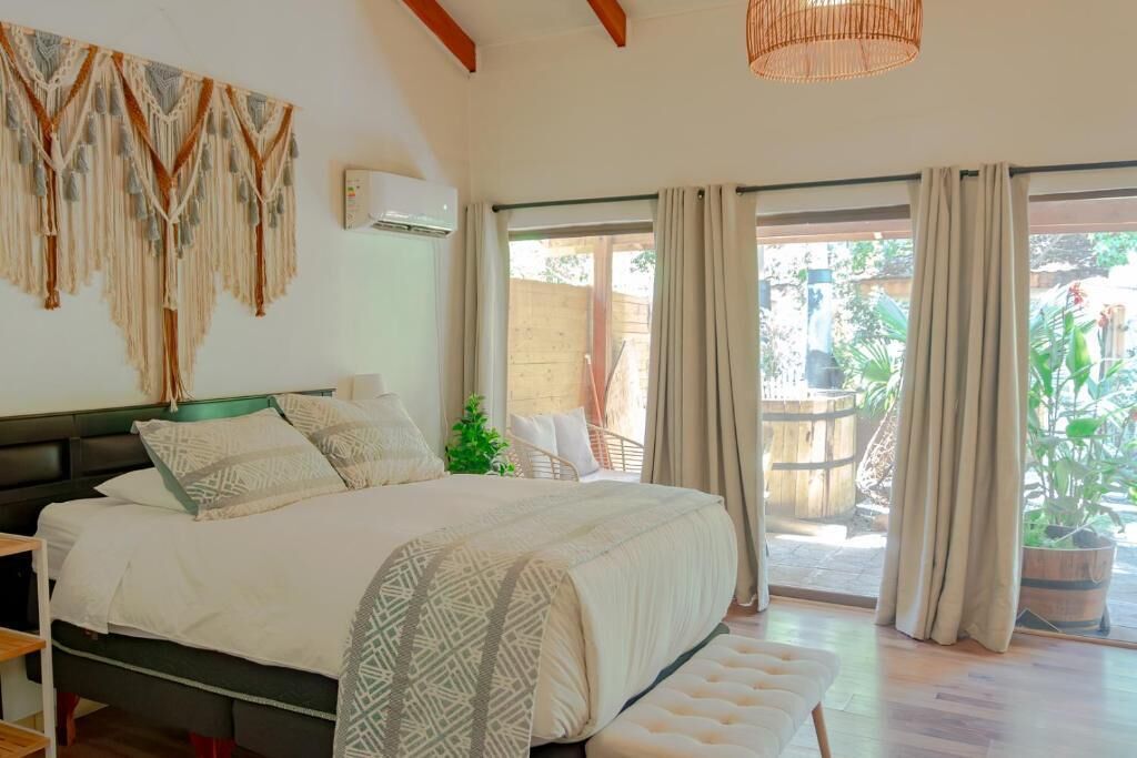 Quarto com cama, mesa de cabeceira, decoração de macramé pendente, janela com cortinas e vista para o exterior.