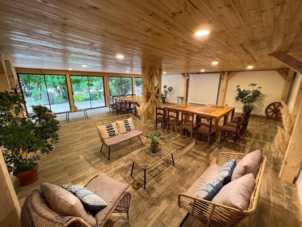 A spacious room with a wooden ceiling, large windows, a dining table, and wicker furniture.