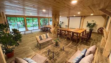 A spacious room with a wooden ceiling, large windows, a dining table, and wicker furniture.