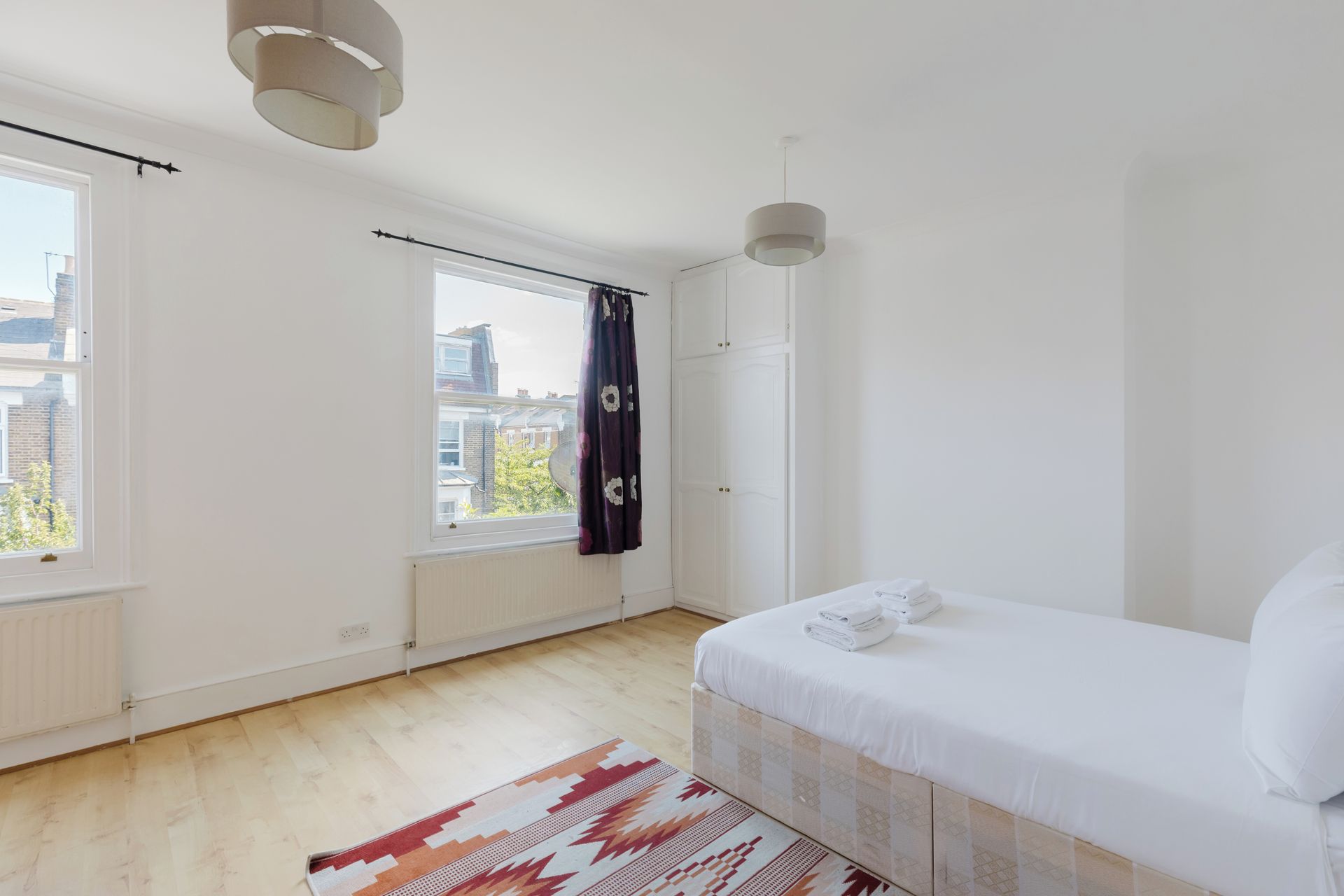 A bedroom with a bed, a window, a radiator, and a door.