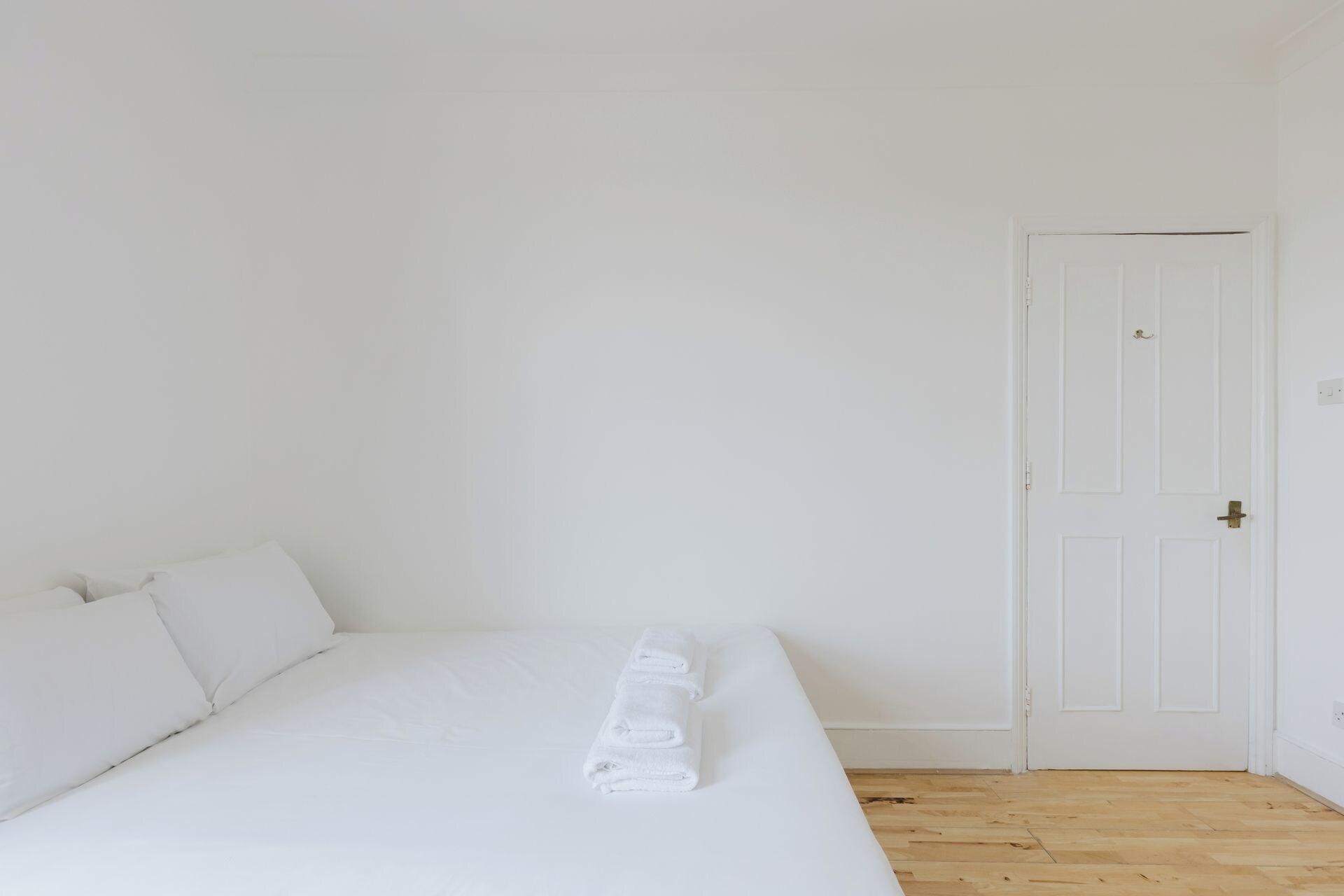 A single-bed room with a wooden floor, white walls, and a closed door.
