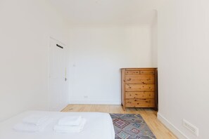 Um quarto com uma cama, uma cômoda de madeira e um tapete estampado.