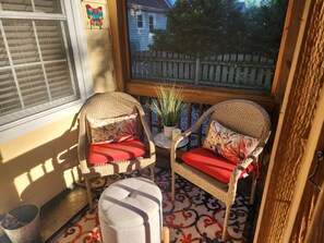 A sunlit room with wicker furniture, a small table with a plant, and a view of a wooden fence and house.