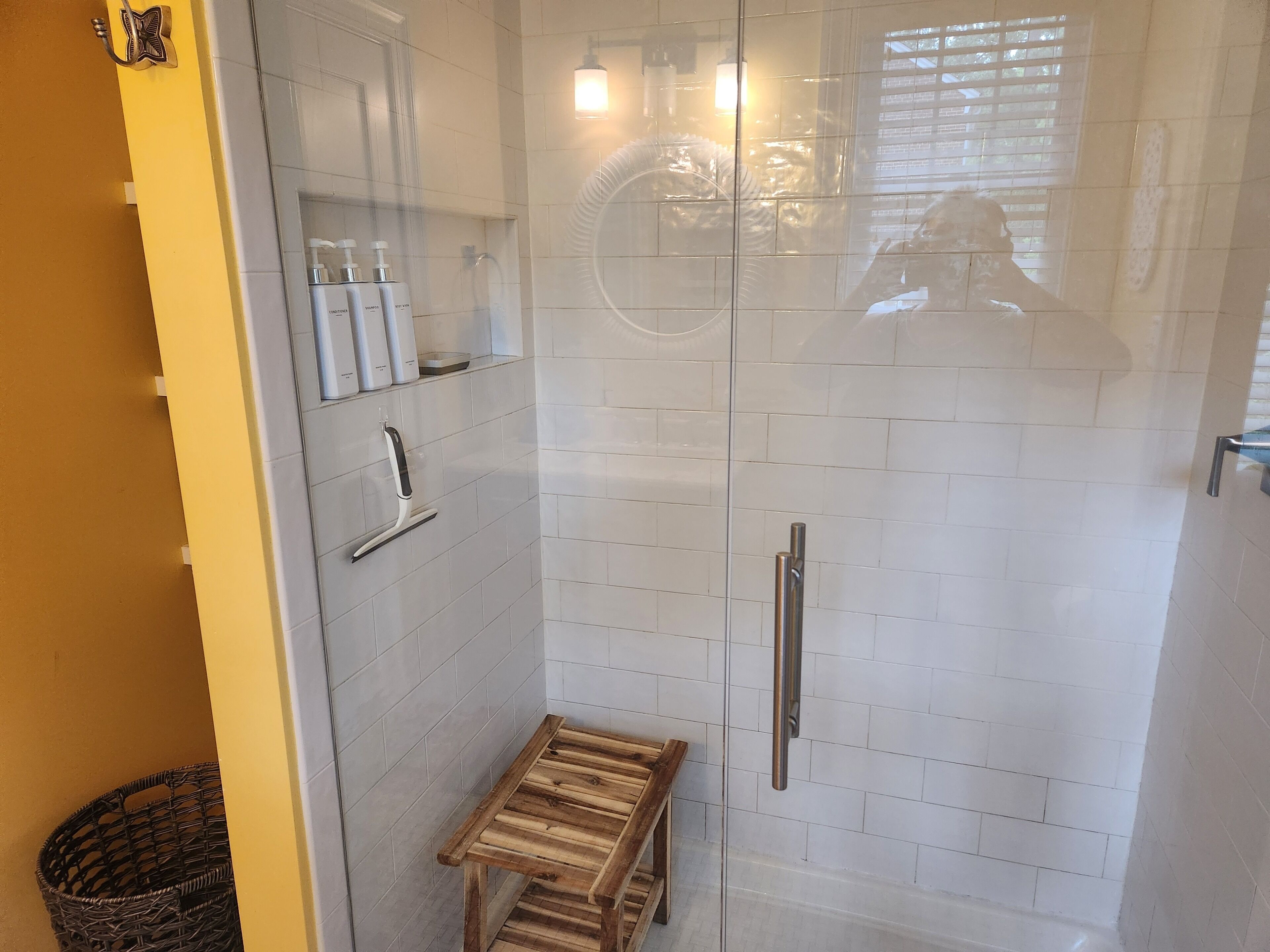Ducha con cerramiento de vidrio, con un banco, un secador de manos y un dispensador de jabón en la pared.