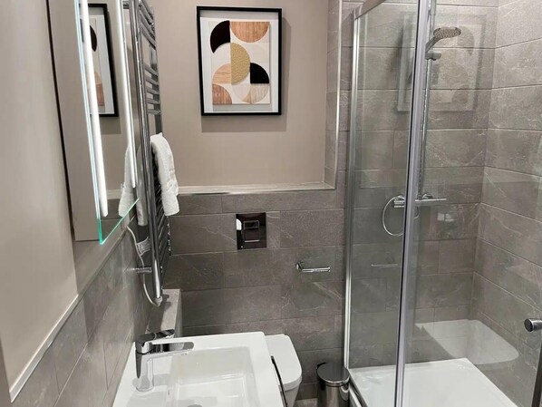 A modern bathroom with a glass shower enclosure, a white sink, and a framed abstract artwork on the wall.