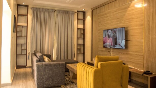 Una sala de estar moderna con un sofá, sillones, una mesa de centro y un televisor montado en una pared de madera.