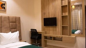 Una habitación de hotel con una cama, un escritorio, una silla, un televisor y un espejo.
