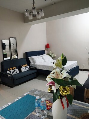 Ein Hotelzimmer mit einem Bett, einem Sofa, einem Spiegel, einer roten Lampe und einer Vase mit Blumen.