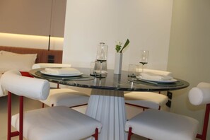Un espace repas moderne avec une table en verre, des chaises à revêtement blanc et un vase rempli de fleurs.