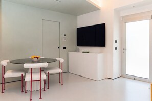 A modern room with a round table, white chairs, a flat-screen TV, and a white cabinet.