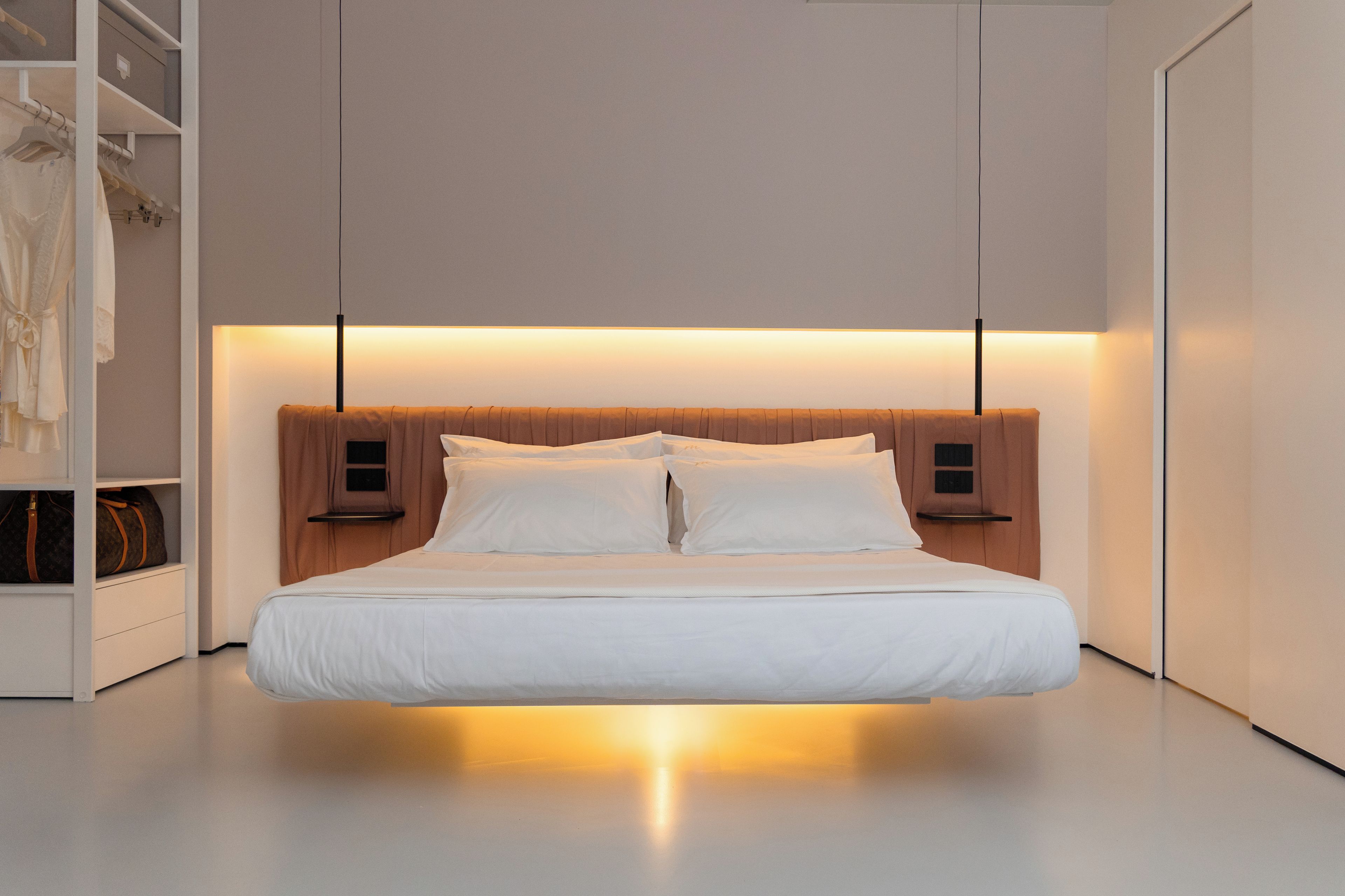 Ein modernes Schlafzimmer mit einem Bett, das unter einem querverlaufenden Kopfteil zentriert ist und von zwei Nachttischen mit Lampen eingerahmt wird.