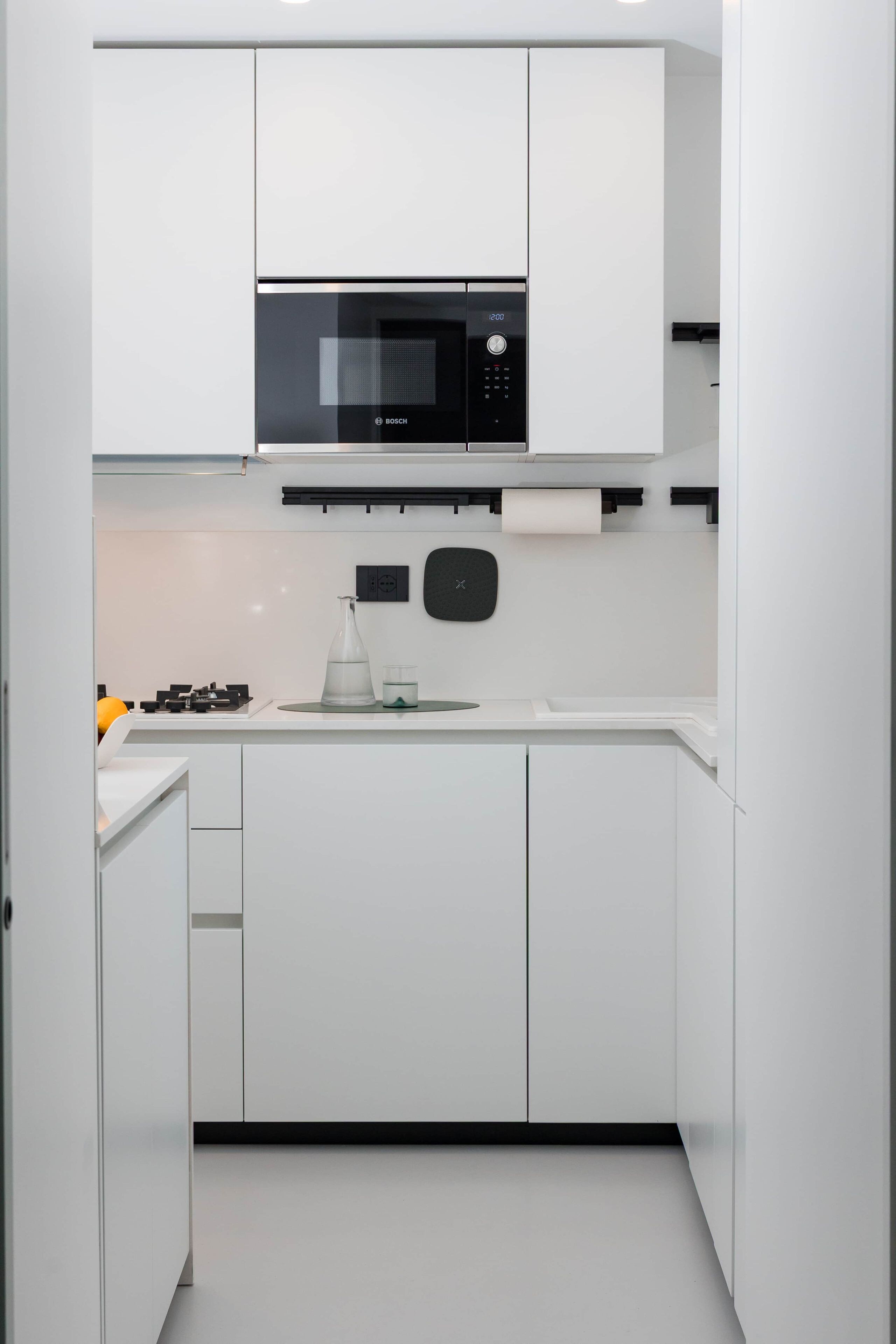 Une cuisine moderne avec des meubles blancs, un four à micro-ondes Bosch, une cuisinière à gaz et une machine à café.