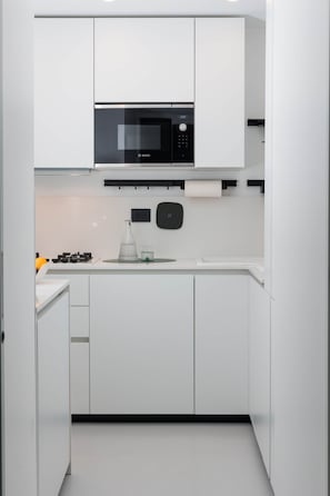 Una cocina moderna con armarios blancos, un microondas Bosch, una estufa a gas y una cafetera.