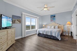 Ein Schlafzimmer mit einem Bett, einem Fernseher, einem Deckenventilator und einem großen Fenster.