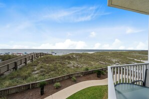 Blick auf einen Strand vom Balkon aus, mit Holzterrasse und Rasenfläche.