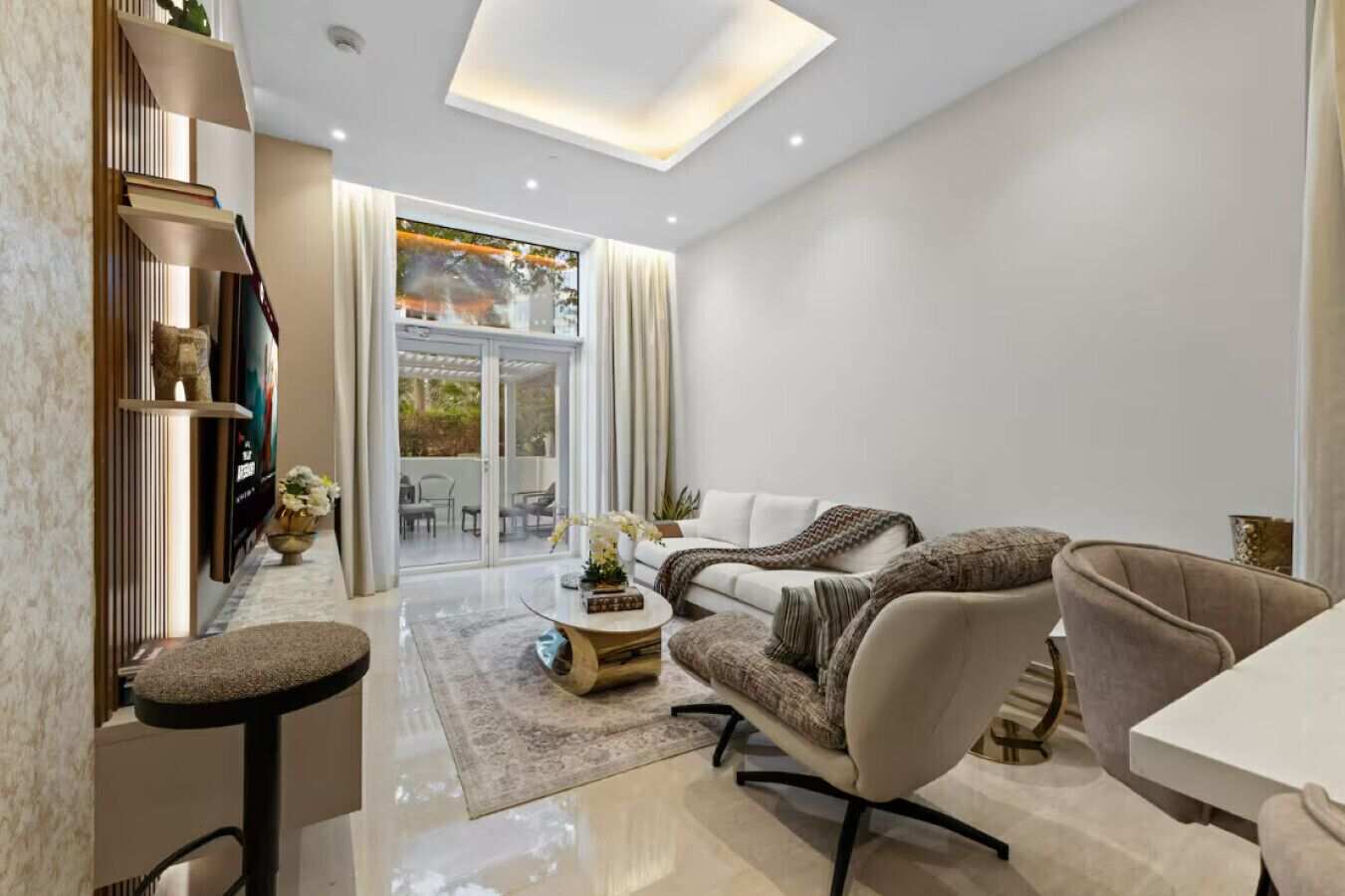 Una sala de estar moderna con sofá, sillones, una mesa de centro y una mesa de comedor. Hay un ventanal corredero que da a un espacio exterior.