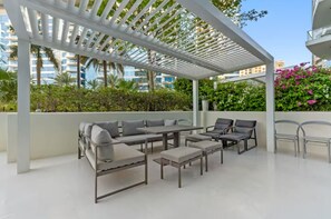 An outdoor patio area with a pergola, seating arrangements, and a view of the surrounding buildings. - Palm Jumeirah 2BR w/ Direct Beach Access (Dubai)