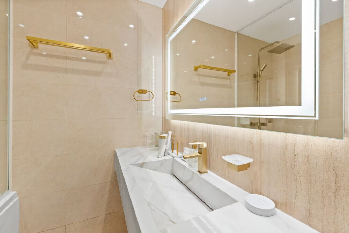 A modern bathroom with a large mirror, a white marble vanity, and gold fixtures.
