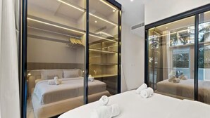 Ein modernes Hotelzimmer mit einem großen Bett, einem begehbaren Kleiderschrank und Blick durch eine Glaswand.