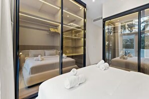 A modern hotel room with a large bed, a walk-in closet, and a view through a glass wall. - Palm Jumeirah 2BR w/ Direct Beach Access (Dubai)