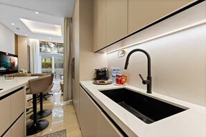 A modern kitchen with a black sink, a coffee machine, and a TV on the wall. - Palm Jumeirah 2BR w/ Direct Beach Access (Dubai)