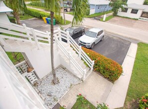 A residential area with a white staircase leading to a balcony, a parked car, and a well-maintained lawn. - 2BR 1BA Renovated Beach Apt in a Small Building (West Palm Beach)