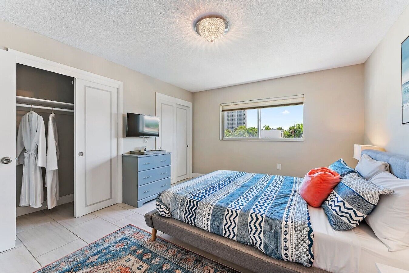 Un dormitorio con cama, televisión, armario y ventana.