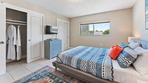 Een slaapkamer met een bed, televisie, kast en raam.