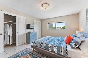 A bedroom with a bed, a TV, a wardrobe, and a window. - 2BR 1BA Renovated Beach Apt in a Small Building (West Palm Beach)