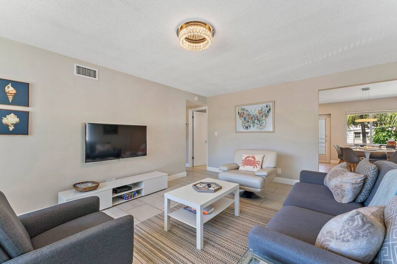 A modern living room with a flat-screen TV, a sofa, a coffee table, and a dining area in the background.