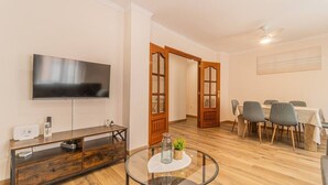 Ein Wohnzimmer mit Flachbildfernseher, einer Holz-Unterhaltungseinrichtung, einem Glastisch und einem Essbereich mit Tisch und Stühlen.