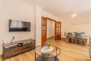 A living room with a flat-screen TV, a wooden entertainment unit, a glass coffee table, and a dining area with a table and chairs. - Explore Zaragoza from the City Center (Zaragoza)