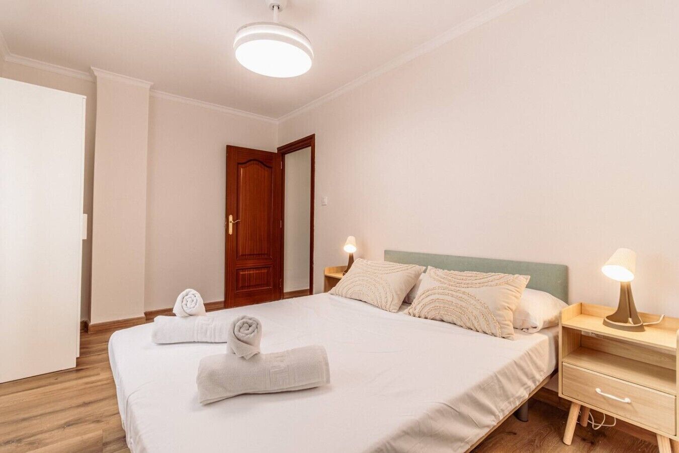 A hotel room with a bed, bedside lamps, a wooden door, and a white wall.