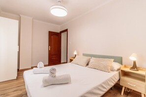 Una habitación de hotel con una cama, lámparas de noche, una puerta de madera y una pared blanca.