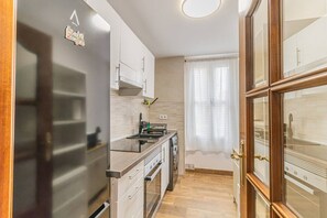 Une cuisine moderne équipée d’un four encastré, d’une cuisinière et d’un évier. Une fenêtre est agrémentée d’un rideau, et la cuisine est dotée d’un plancher en bois.