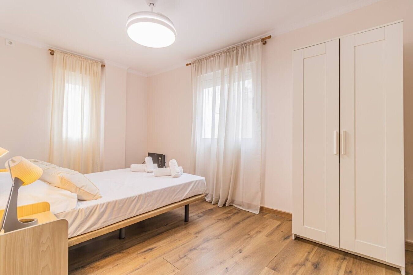 A bedroom with a single bed, a bedside table with a lamp, a wardrobe, and a window with curtains.