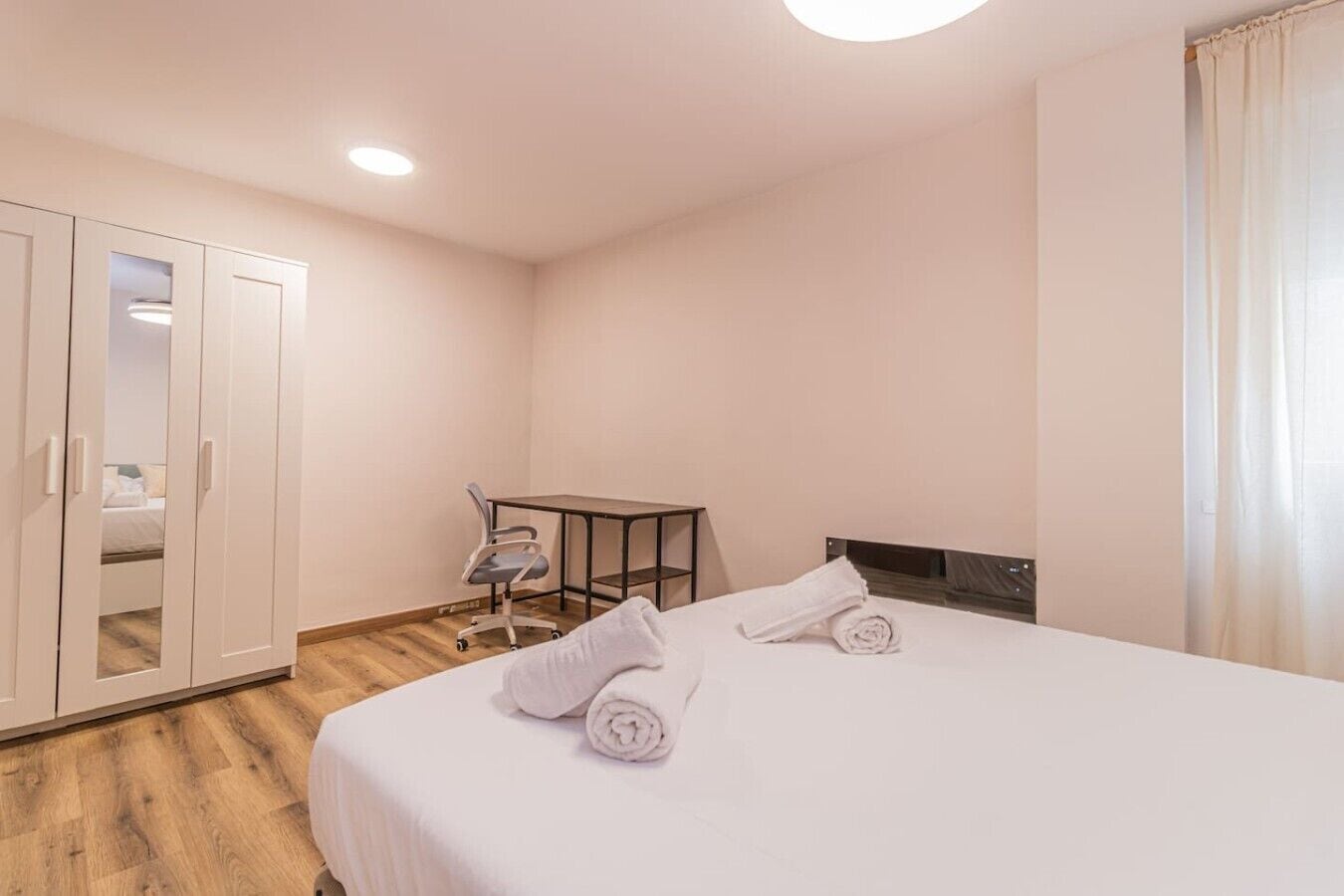 A hotel room with a bed, a desk, a chair, and a wardrobe.