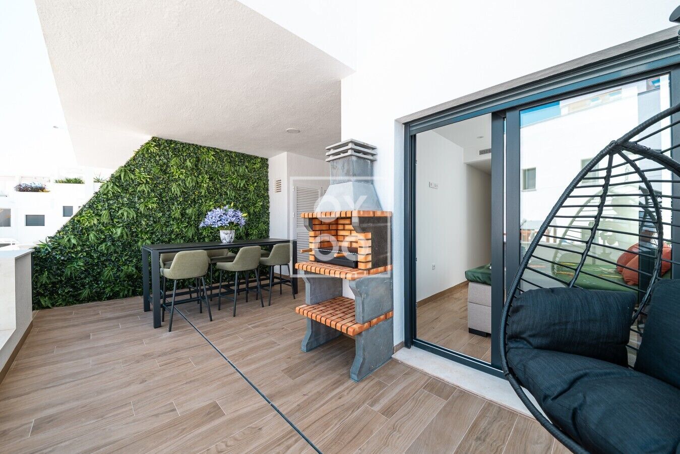 A modern outdoor dining area with a brick barbecue grill, a dining table with chairs, and a green wall.
