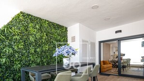 Un comedor moderno con una mesa y sillas de madera oscura, una pared cubierta de follaje verde y vista a una zona de cocina.