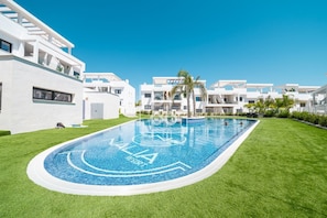 A modern pool area with a clear blue pool, surrounded by well-maintained grass and white buildings. - Casa de Adamant - Ground floor resort apartment with BBQ, shared jacuzzi and pool by OYOOSTAYS (Torrevieja)