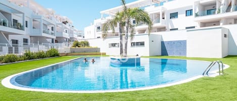 A modern residential building with a swimming pool surrounded by well-maintained grass.