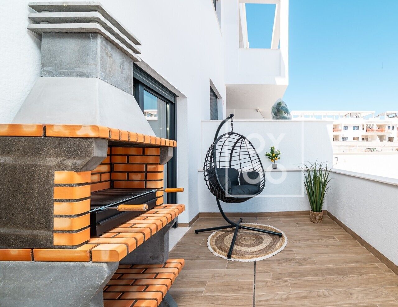 A rooftop terrace with a brick barbecue, a hanging chair, and a potted plant.