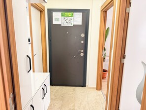 En hall med en mörk dörr, trädörrar på vardera sidan och ett klinkergolv.