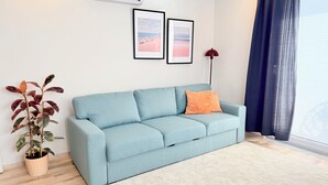 A light blue sofa with an orange pillow, a potted plant, and two framed pictures on the wall. - Modern Central Flat Near Old Town with Fast WiFi 2BR (ANTALYA)